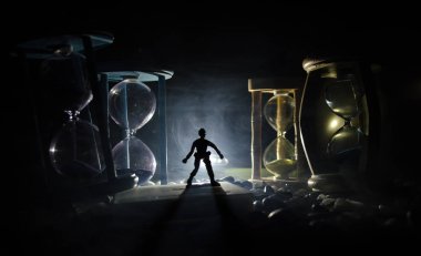 Zaman kavramı. Duman ile hourglasses ve karanlık bir arka plan ışıkları arasında duran bir adam silüeti.