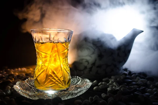 Turkish Azerbaijan tea in traditional glasse and pot on black background with lights and smoke. Armudu traditional cup