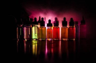 Vape konsepti. Karanlık arka planda duman bulutları ve tüp sıvısı şişeleri. Işık efektleri. Arka plan, vape reklamı ya da vape arkaplan olarak kullanışlı. Seçici odak