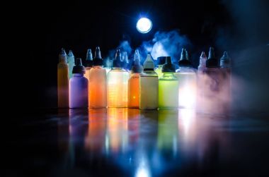 Vape konsepti. Karanlık arka planda duman bulutları ve tüp sıvısı şişeleri. Işık efektleri. Arka plan, vape reklamı ya da vape arkaplan olarak kullanışlı. Seçici odak