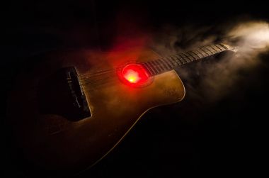 Müzik konsepti. Akustik gitar ile kopya alanı dumanla ışık demeti altında karanlık bir arka plan üzerinde izole. Gitar telleri, yakın çekim. Seçici odak. Yangın etkileri