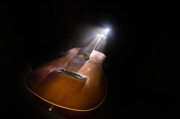 Music concept. Acoustic guitar isolated on a dark background under beam of light with smoke with copy space. Guitar Strings, close up. Selective focus. Fire effects