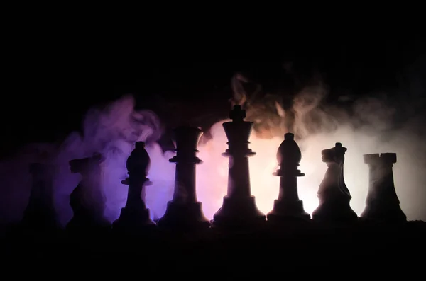Концепция шахматной настольной игры бизнес-идей, конкуренции и стратегических идей. Шахматные фигуры на темном фоне с дымом и туманом — стоковое фото