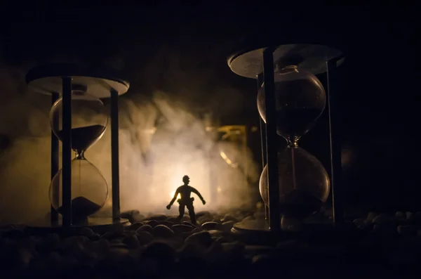 Tid koncept. Silhuetten av en man som stod mellan timglas med rök och ljus på en mörk bakgrund. — Stockfoto