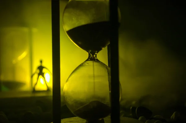 Concept du temps. Silhouette d'un homme debout entre des sabliers avec de la fumée et des lumières sur un fond sombre . — Photo