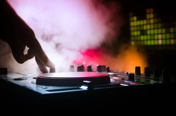 DJ Spinning, Mixing, and Scratching in a Night Club, Manos de dj ajustar varios controles de pista en la cubierta de dj, luces estroboscópicas y niebla, enfoque selectivo — Foto de Stock