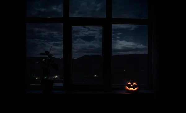 Enge Halloween pompoen in het venster van de mystieke huis bij nacht of halloween pompoen in nacht op kamer met blauwe venster. Symbool van halloween in venster. — Stockfoto
