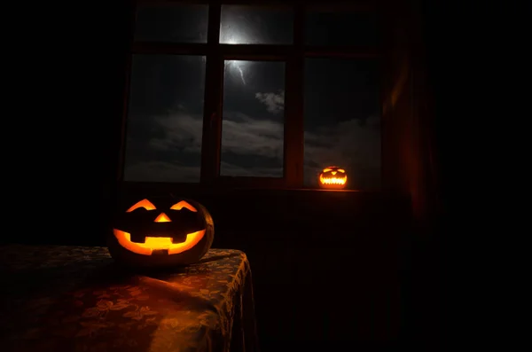 Scary Halloween pumpkin in the mystical house window at night or halloween pumpkin in night on room with blue window. Symbol of halloween in window.