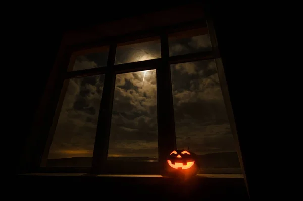 Scary Halloween pumpkin in the mystical house window at night or halloween pumpkin in night on room with blue window. Symbol of halloween in window. — Stock Photo, Image