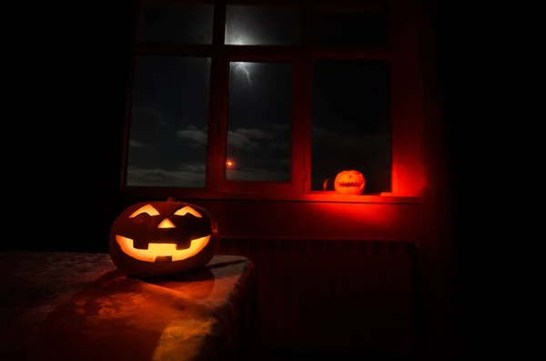 Scary Halloween pumpkin in the mystical house window at night or halloween pumpkin in night on room with blue window. Symbol of halloween in window.