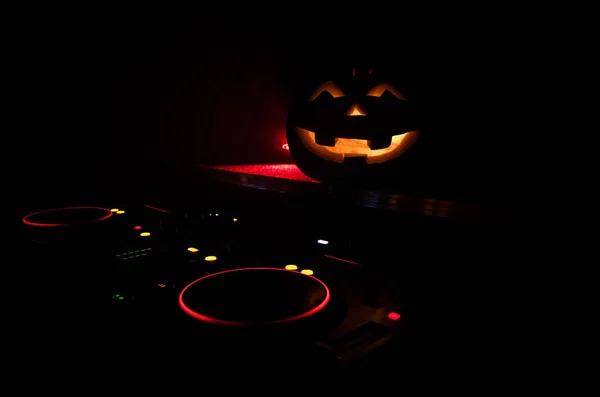 Halloween pumpkin on a dj table with headphones on dark background with copy space. Happy Halloween festival decorations and music concept. Toned