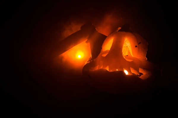 Zucca arancione spaventosa con occhi scolpiti e un sorriso con candele accese e un'ascia su uno sfondo scuro con cielo di fuoco. Per la festa di Halloween. Spazio vuoto . — Foto Stock