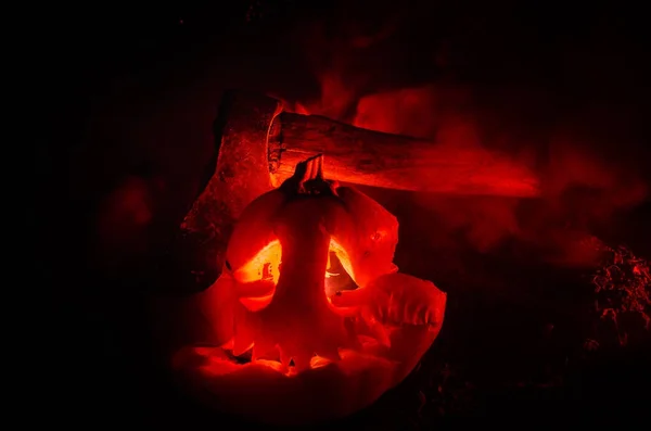 Scary orange pumpkin with carved eyes and a smile with burning candles and an ax on a dark background with fire sky. For the Halloween party. Empty space. — Stock Photo, Image