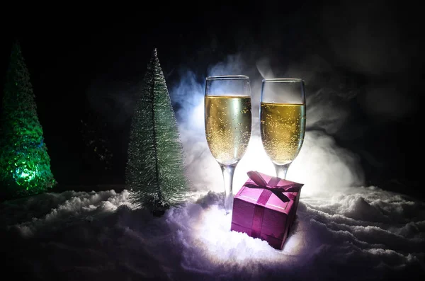 Capodanno celebrazione sfondo con coppia di flauti e bottiglia di champagne con albero di Natale sulla neve su sfondo scuro . — Foto Stock