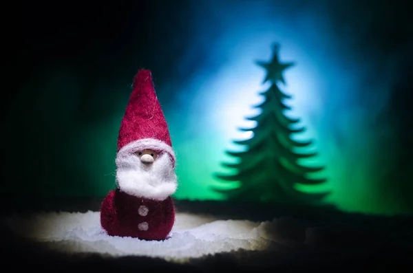 Szczęśliwy lalka Santa Claus na Boże Narodzenie w drzewa i śnieg. Bokeh kolorowe tło. Śnięty Mikołaj i Wesołych Świąt zabawka rysunek modelu na ciemnym stonowanych — Zdjęcie stockowe