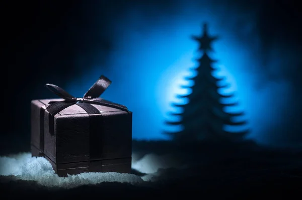 Caja de regalo roja de Navidad y abeto en la nieve. Decoración de la casa de Navidad con nieve y árbol sobre un fondo oscuro con espacio para copiar — Foto de Stock