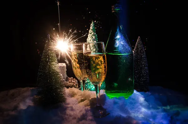 Fondo de celebración de Nochevieja con un par de flautas y una botella de champán con árbol de Navidad sobre nieve sobre fondo oscuro . — Foto de Stock