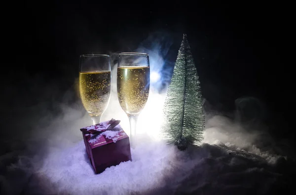 Capodanno celebrazione sfondo con coppia di flauti e bottiglia di champagne con albero di Natale sulla neve su sfondo scuro . — Foto Stock