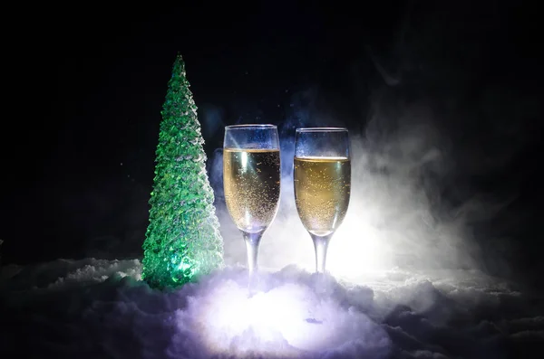 Capodanno celebrazione sfondo con coppia di flauti e bottiglia di champagne con albero di Natale sulla neve su sfondo scuro . — Foto Stock