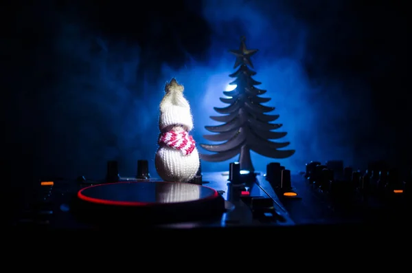 Dj mixer with headphones on dark nightclub background with Christmas tree New Year Eve. Close up view of New Year elements or symbols (Santa Clause, Snowman, Dog 2018, gift box) on a Dj table. toned