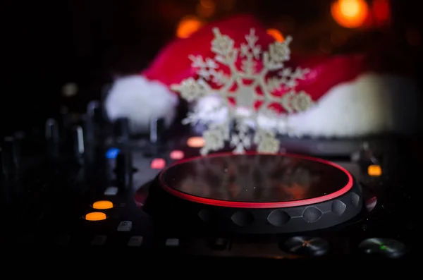 Dj mixer with headphones on dark nightclub background with Christmas tree New Year Eve. Close up view of New Year elements or symbols (Santa Clause, Snowman, Dog 2018, gift box) on a Dj table. toned