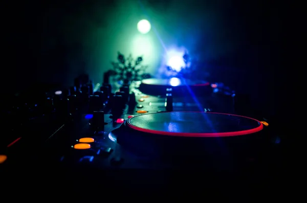 Mezclador de DJ con auriculares en el fondo oscuro club nocturno con árbol de Navidad Nochevieja. Vista de cerca de los elementos o símbolos de Año Nuevo (Santa Claus, muñeco de nieve, perro 2018, caja de regalo) en una mesa de Dj. tonificado —  Fotos de Stock