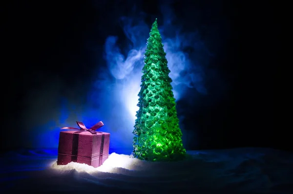 Κόκκινο Χριστουγεννιάτικο δώρο κουτί και fir tree στο χιόνι. Χριστουγεννιάτικη διακόσμηση σπιτιού με χιόνι και το δέντρο σε σκούρο φόντο με αντίγραφο χώρου — Φωτογραφία Αρχείου