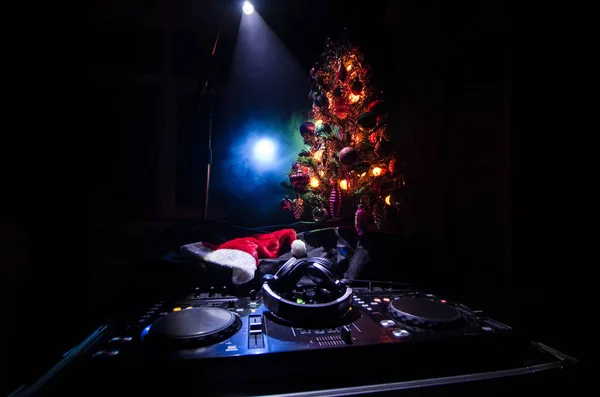 Dj mixer with headphones on dark nightclub background with Christmas tree New Year Eve. Close up view of New Year elements or symbols (Santa Clause, Snowman, Dog 2018, gift box) on a Dj table. toned