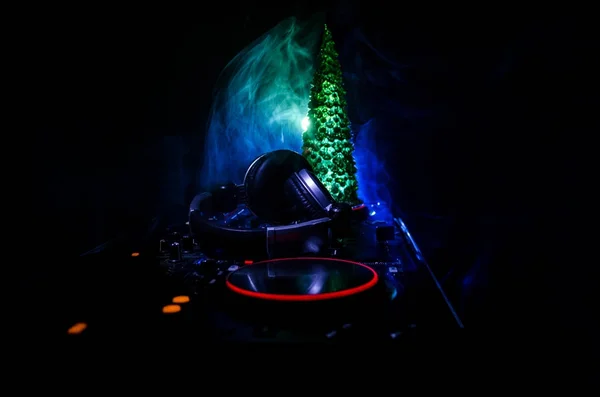 Dj mixer with headphones on dark nightclub background with Christmas tree New Year Eve. Close up view of New Year elements or symbols (Santa Clause, Snowman, Dog 2018, gift box) on a Dj table. toned — Stock Photo, Image
