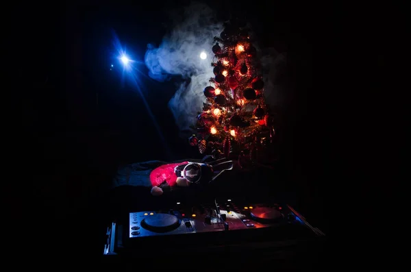 Dj mixer with headphones on dark nightclub background with Christmas tree New Year Eve. Close up view of New Year elements or symbols (Santa Clause, Snowman, Dog 2018, gift box) on a Dj table. toned