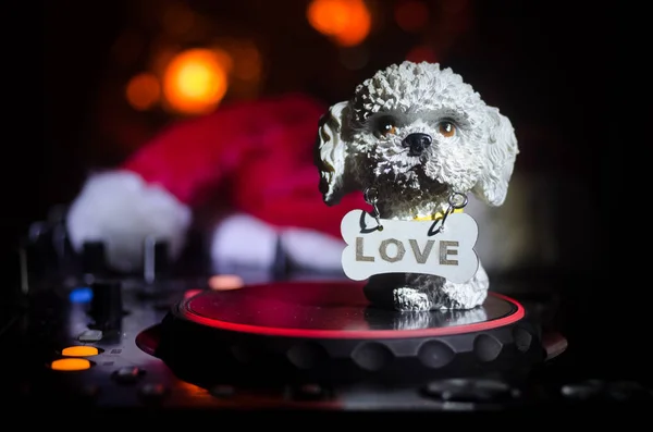 Dj mixer with headphones on dark nightclub background with Christmas tree New Year Eve. Close up view of New Year elements or symbols (Santa Clause, Snowman, Dog 2018, gift box) on a Dj table. toned