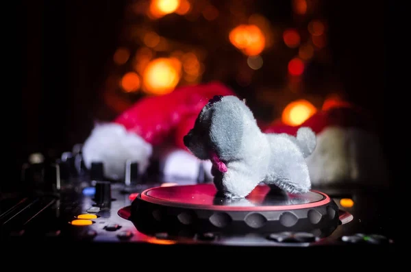 Dj mixer with headphones on dark nightclub background with Christmas tree New Year Eve. Close up view of New Year elements or symbols (Santa Clause, Snowman, Dog 2018, gift box) on a Dj table. toned