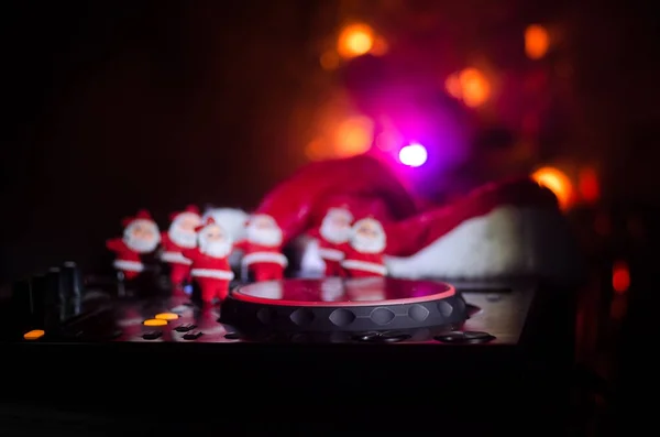 Dj mixer with headphones on dark nightclub background with Christmas tree New Year Eve. Close up view of New Year elements or symbols (Santa Clause, Snowman, Dog 2018, gift box) on a Dj table. toned