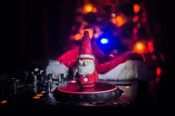 Dj mixer with headphones on dark nightclub background with Christmas tree New Year Eve. Close up view of New Year elements or symbols (Santa Clause, Snowman, Dog 2018, gift box) on a Dj table. toned