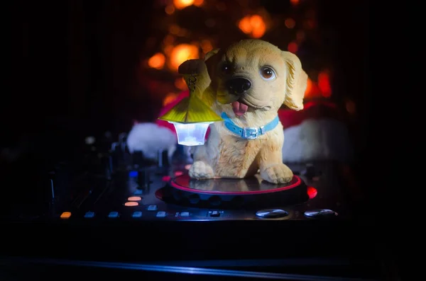 Dj mixer with headphones on dark nightclub background with Christmas tree New Year Eve. Close up view of New Year elements or symbols (Santa Clause, Snowman, Dog 2018, gift box) on a Dj table. toned