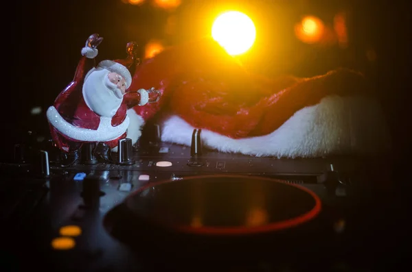 Dj mixer with headphones on dark nightclub background with Christmas tree New Year Eve. Close up view of New Year elements or symbols (Santa Clause, Snowman, Dog 2018, gift box) on a Dj table. toned