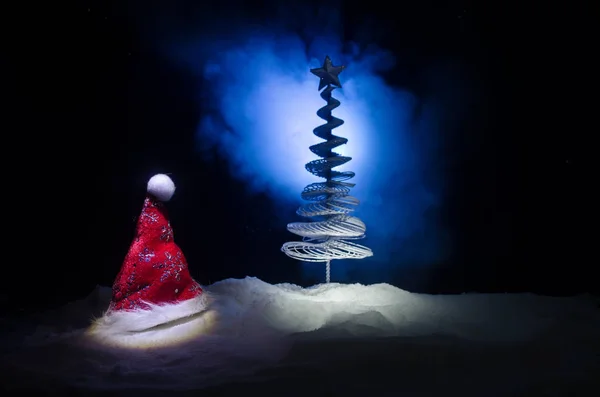 Noël vacances Nouvel An fond avec chapeau Santa Clause et arbre de Noël flou sur fond neigeux. Décoration d'image conceptuelle Nouvel An avec des attributs de vacances. Fond ton foncé — Photo