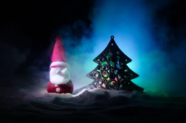 Glückliche Weihnachtsmann-Puppe zu Weihnachten mit Baum und Schnee. bunte Bokeh Hintergrund. Weihnachtsmann-Klausel und frohe Weihnachten Modell Figur Spielzeug auf dunkel getönten nebligen Hintergrund — Stockfoto