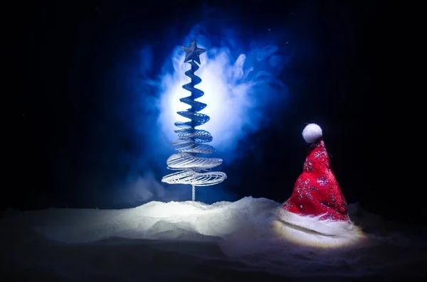 Рождественский праздник Новый год фон с шляпой Санта-Клауса и размытые елки на снежном фоне. Новогоднее концептуальное оформление с атрибутами праздника. Тёмный фон — стоковое фото