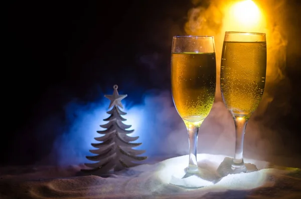 Sylwestra tło uroczystość z pary fletów i butelkę szampana z atrybuty Bożego Narodzenia (lub elementy) na snowy ciemny stonowanych mglisty tło. Selektywny fokus. — Zdjęcie stockowe