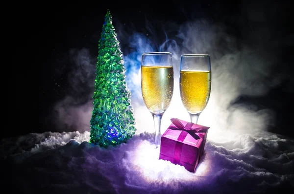 Szilveszteri ünneplés háttér pár fuvolák és üveg pezsgőt, karácsonyfa, a hó, a sötét háttér. — Stock Fotó