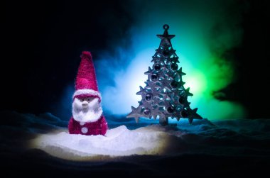 Mutlu Noel baba bebek ağaç ve kar ile Noel zamanında. Renkli bokeh arka plan. Noel Baba ve mutlu Noeller modeli şekil oyuncak koyu tonda sisli arka plan üzerinde