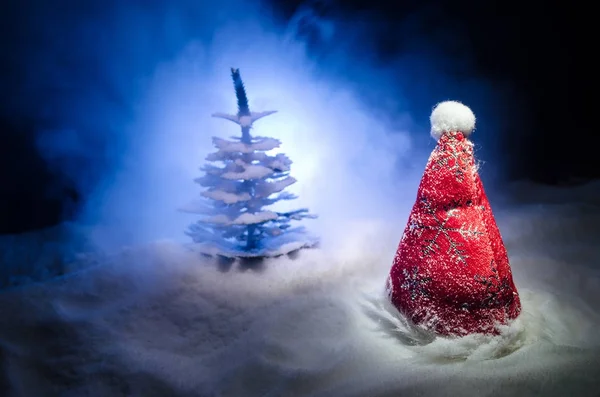 Рождественский праздник Новый год фон с шляпой Санта-Клауса и размытые елки на снежном фоне. Новогоднее концептуальное оформление с атрибутами праздника. Тёмный фон — стоковое фото