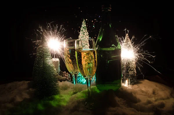 Fondo de celebración de Nochevieja con un par de flautas y una botella de champán con árbol de Navidad sobre nieve sobre fondo oscuro . — Foto de Stock