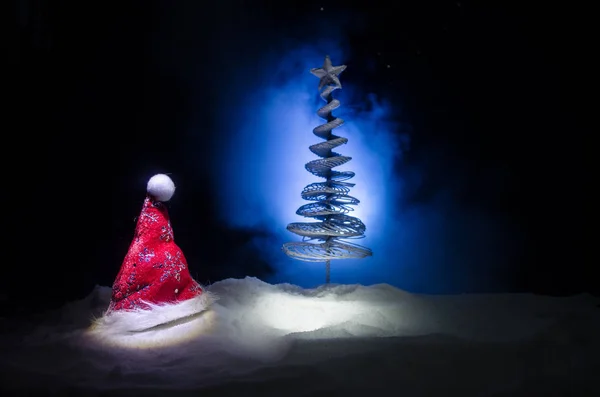 Noël vacances Nouvel An fond avec chapeau Santa Clause et arbre de Noël flou sur fond neigeux. Décoration d'image conceptuelle Nouvel An avec des attributs de vacances. Fond ton foncé — Photo