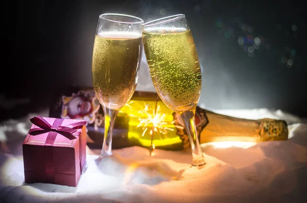 Capodanno sfondo celebrazione con coppia di flauti e bottiglia di champagne con attributi di Natale (o elementi) su sfondo nebbioso scuro nevoso tonica. Focus selettivo . — Foto Stock