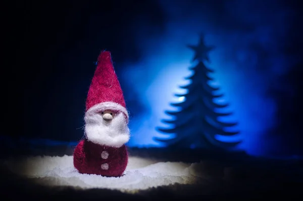 Szczęśliwy lalka Santa Claus na Boże Narodzenie w drzewa i śnieg. Bokeh kolorowe tło. Śnięty Mikołaj i Wesołych Świąt zabawka rysunek modelu na ciemnym stonowanych — Zdjęcie stockowe