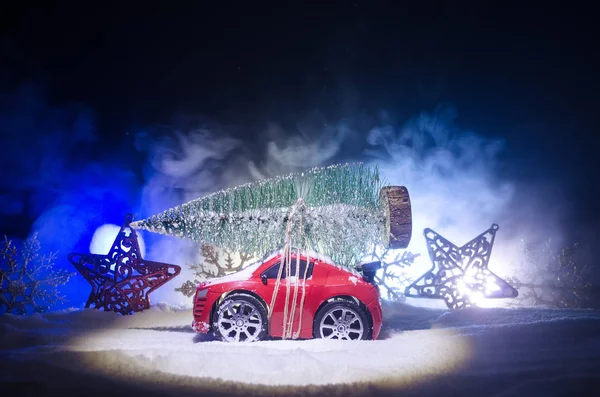 Miniatur-Auto mit Tanne auf schneebedecktem Wintervorland oder Spielzeugauto mit Weihnachtsbaum und nachts — Stockfoto