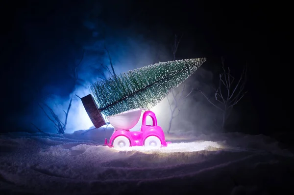 Miniatur-Auto mit Tanne auf schneebedecktem Wintervorland oder Spielzeugauto mit Weihnachtsbaum und nachts — Stockfoto