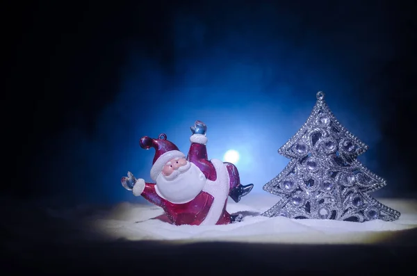 Feliz muñeco de Papá Noel en Navidad con árbol y nieve. Fondo bokeh colorido. Santa Claus y Feliz Navidad modelo figura juguete en oscuro tonificado niebla fondo . — Foto de Stock